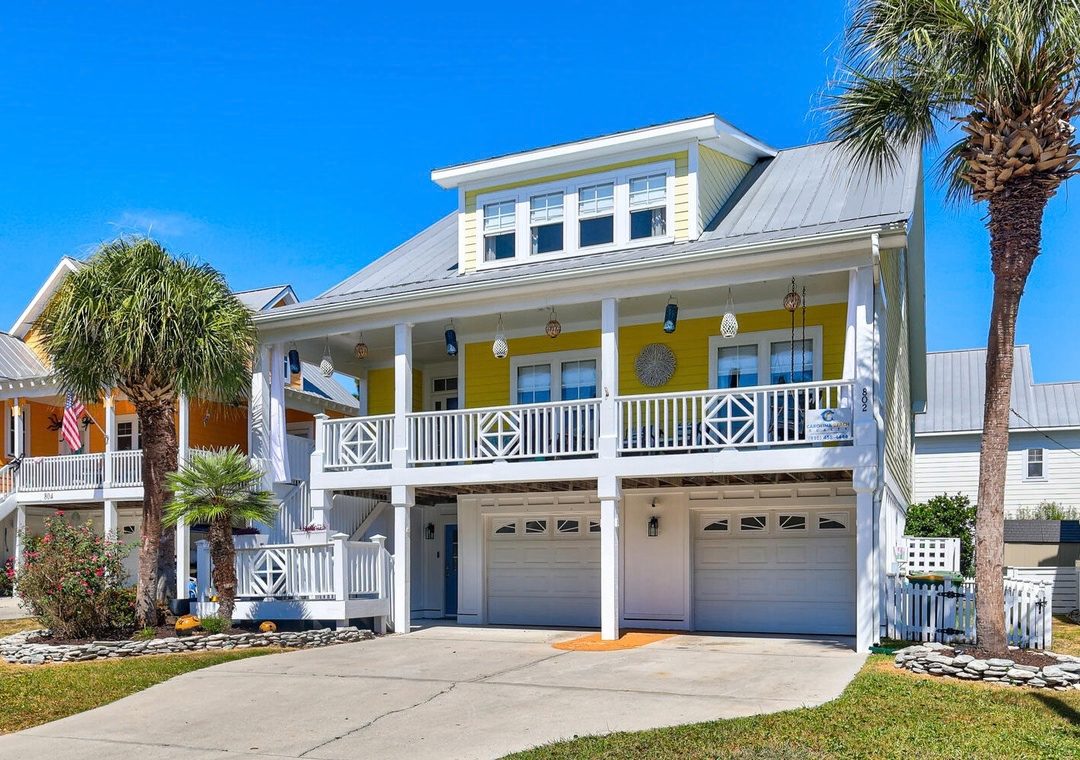 A yellow beach house with white railings and palm trees